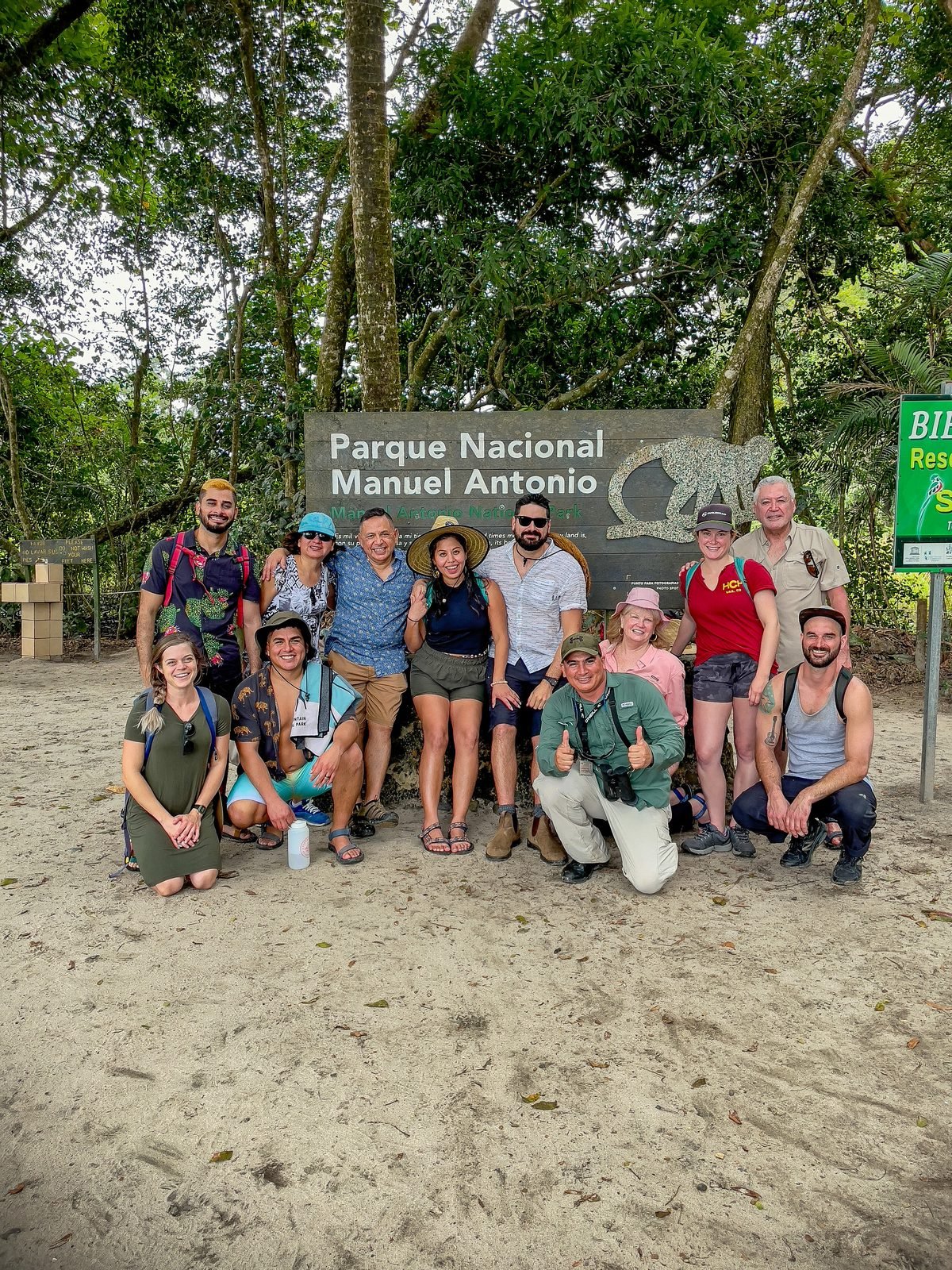 Happy tour group at the Manuel Antonio National Park entrance sign with their Wakoo Tours guide