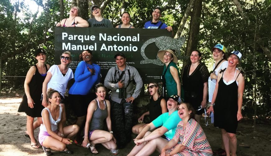 Large group of friends laughing around the Manuel Antonio National Park entrance sign