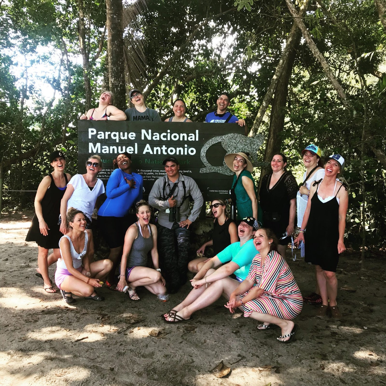 Large group of friends laughing around the Manuel Antonio National Park entrance sign